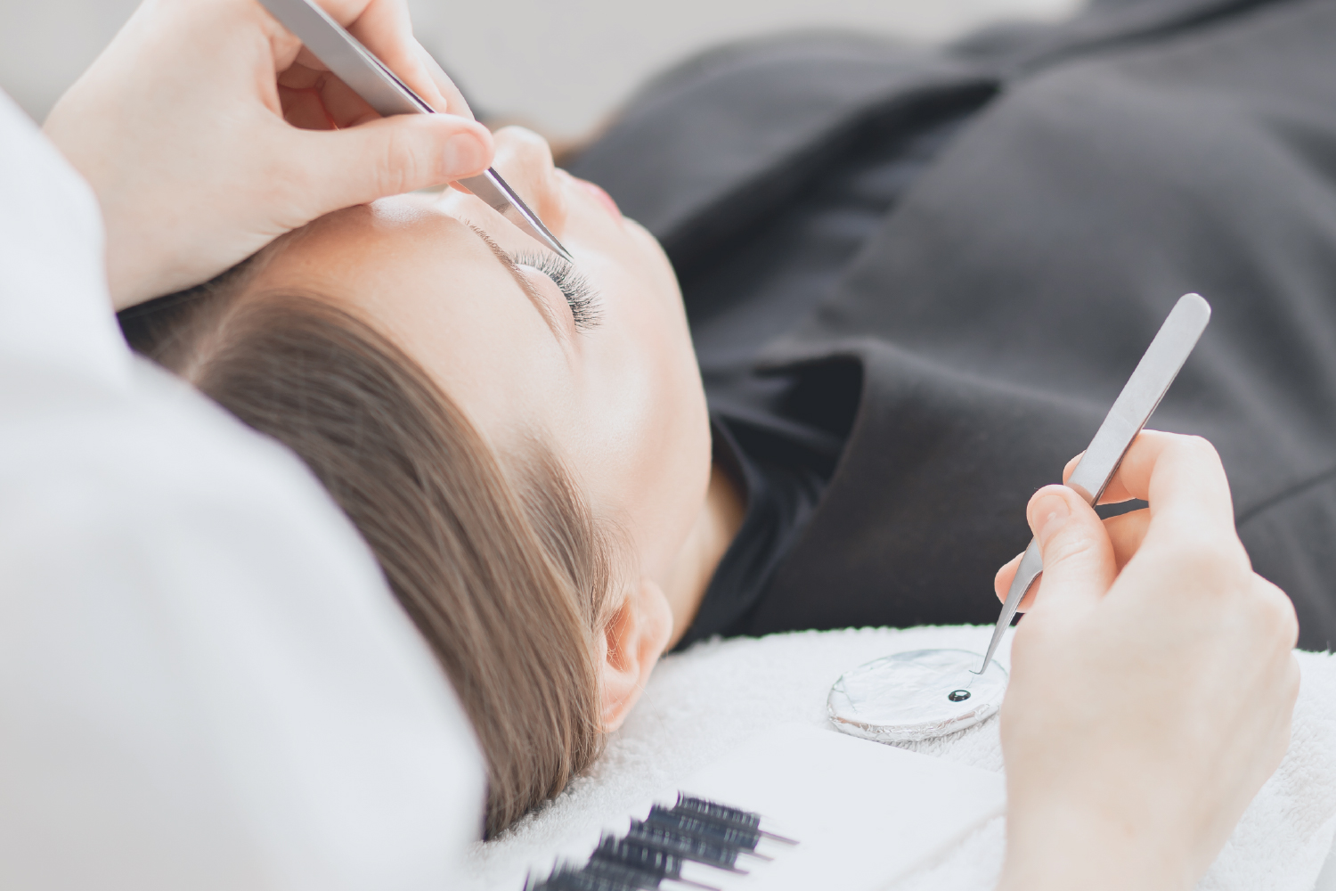 rofessional eyelash extension technician applying lashes with tweezers
