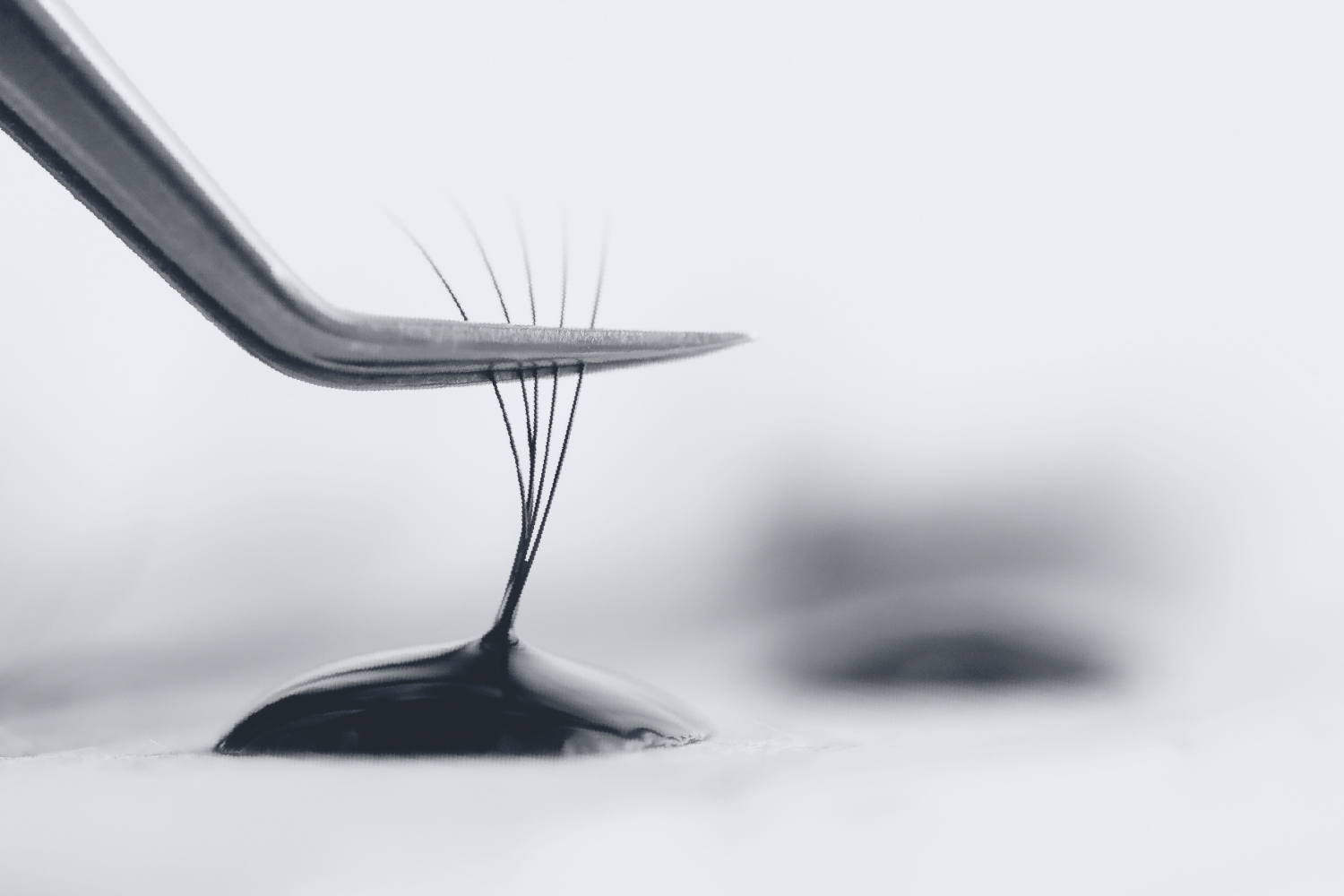 Eyelash extension tweezers dipped into adhesive drop showing perfect glue viscosity