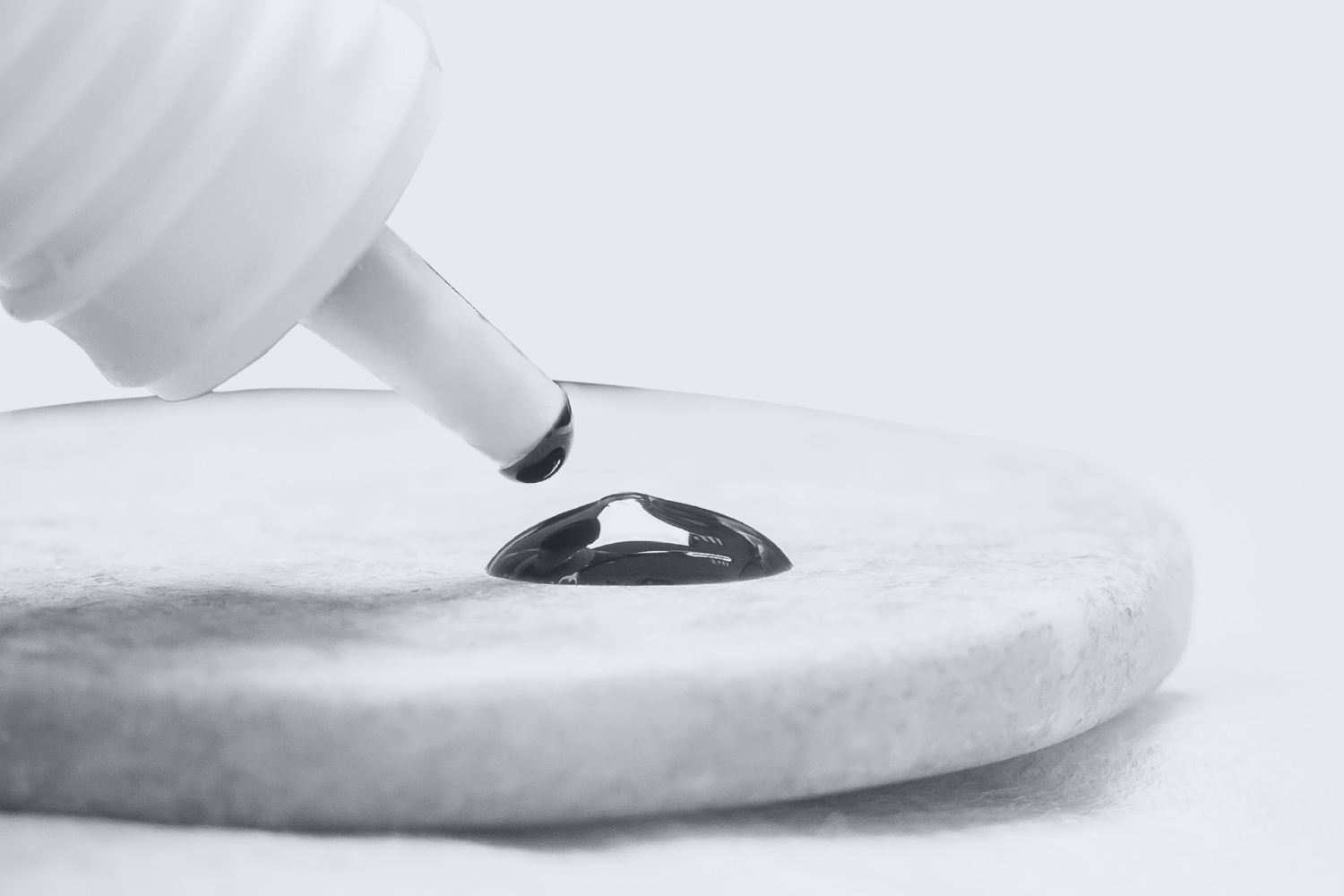 Precision drop of eyelash glue from bottle onto stone palette showing user-friendly packaging