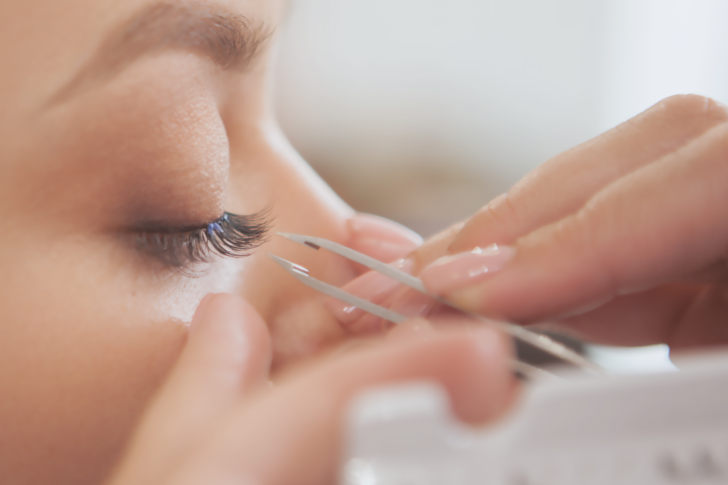 Asian lash artist applying individual lash extension using tweezers - demonstrating high retention and waterproof performance for OEM/ODM lash glue.