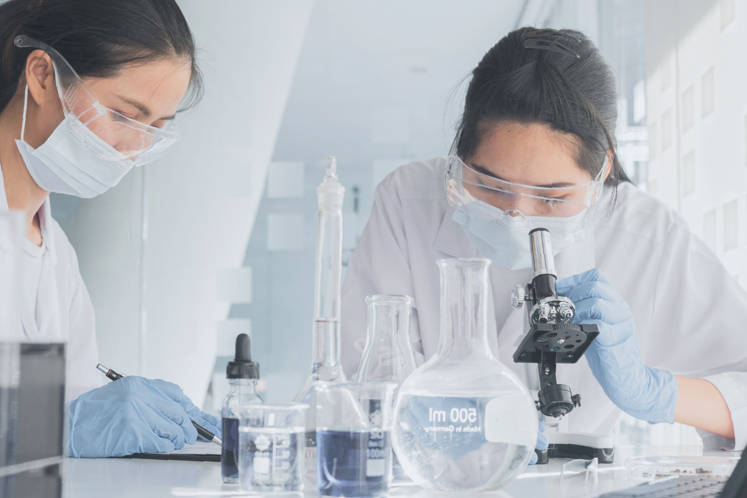 Scientists working in cleanroom lab with beakers and microscope - indicating OEM/ODM lash glue produced under ISO/GMP standards and strict quality control.