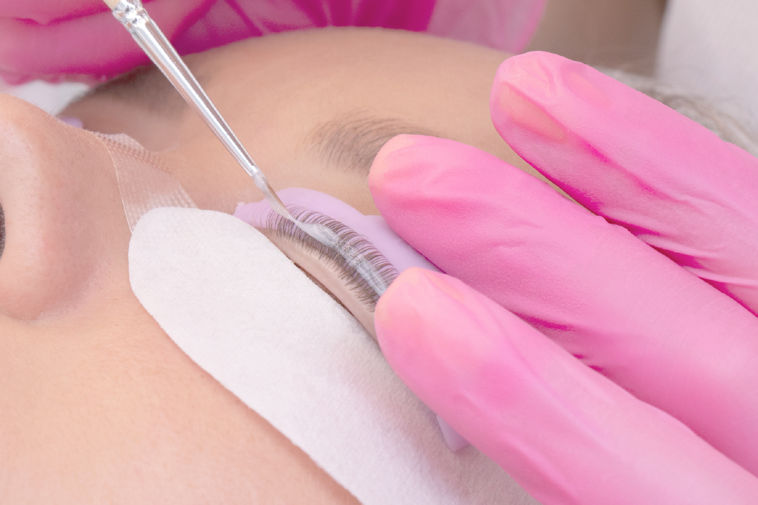 Lash lift softener being brushed onto eyelashes during a keratin lash lift treatment, shown with detailed eye protection.