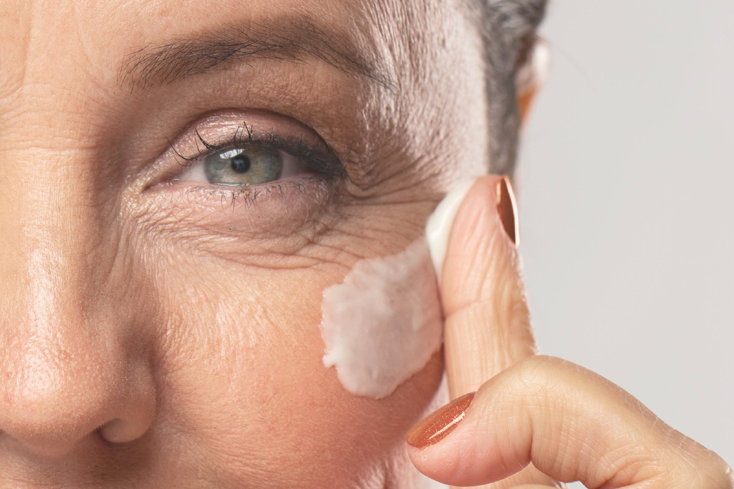 Woman applying anti-aging cream to under-eye area, highlighting deep repair benefits.